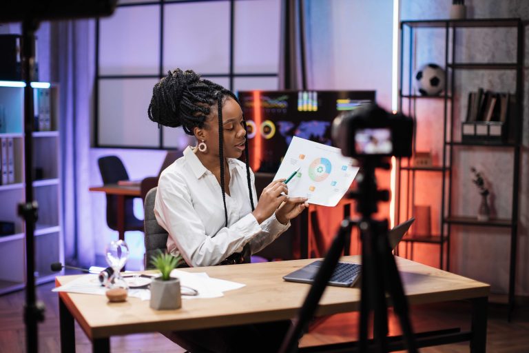African businesswoman in formal suit sitting in front of camera on tripod in evening office