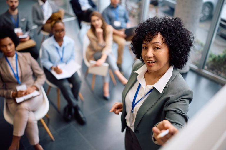 Happy mature businesswoman talking to group of seminar attendees in board room
